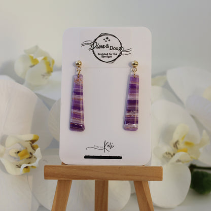 Pair of purple earrings on a display card with floral background