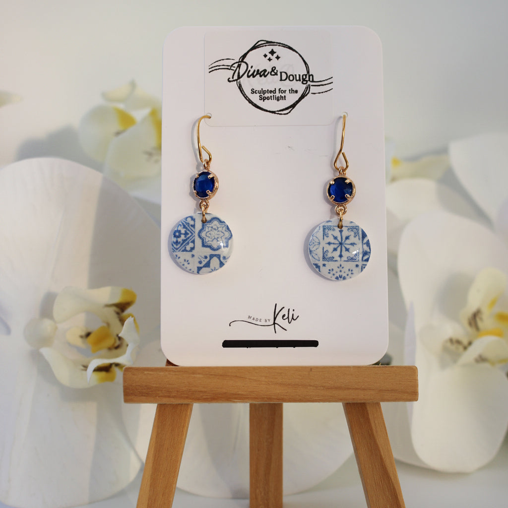 Pair of earrings on a display card with a wooden stand against a white background
