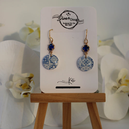 Pair of earrings on a display card with a wooden stand against a white background