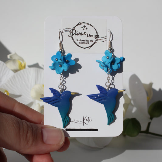Blue bird-shaped earrings on a branded card held by a hand with a white background.