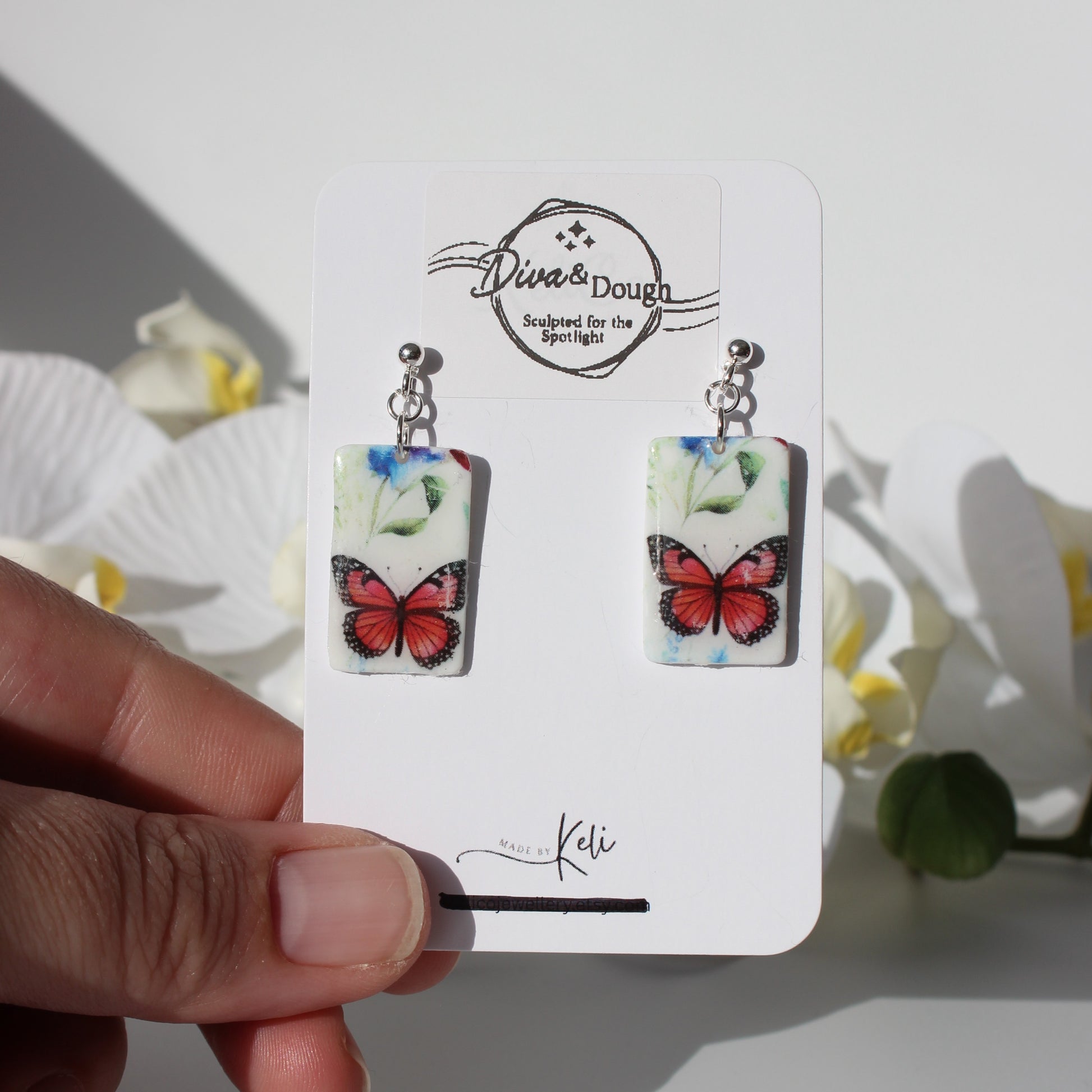 Butterfly earrings on a branded card held by a hand with a white background