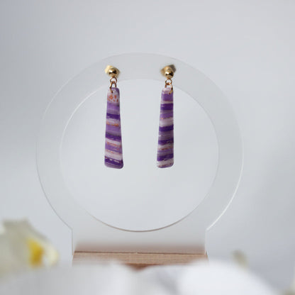 Pair of purple striped earrings on a white stand with a light background