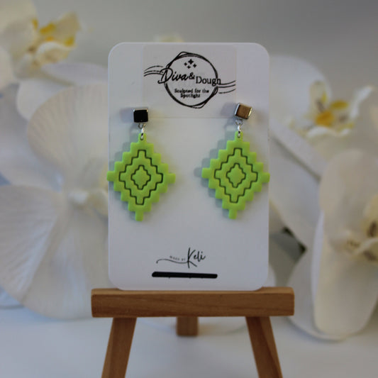 Green geometric earrings on a display card with a wooden stand, white flowers in the background