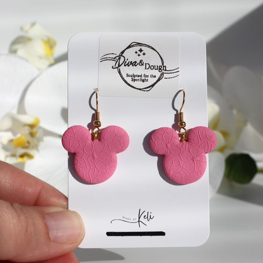 Pink mouse ear earrings on a branded card held by a hand with a white background