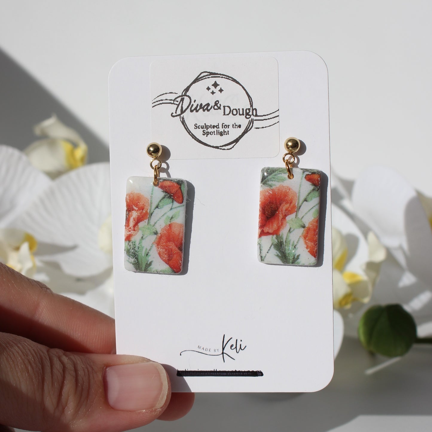 Poppy print earrings on a branded card held by a hand with a natural background