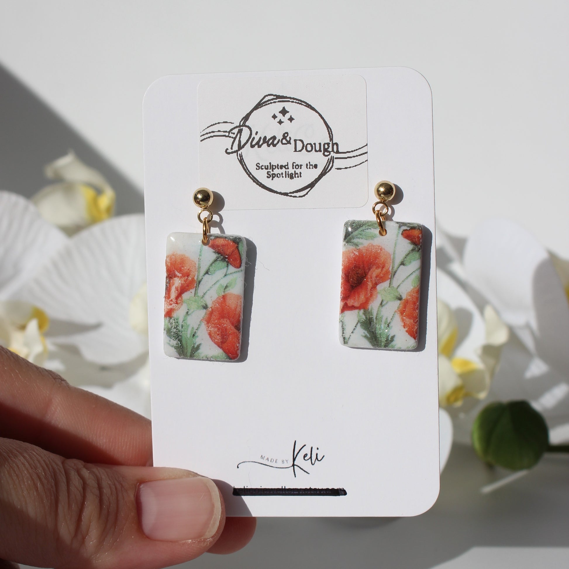 Poppy print earrings on a branded card held by a hand with a natural background