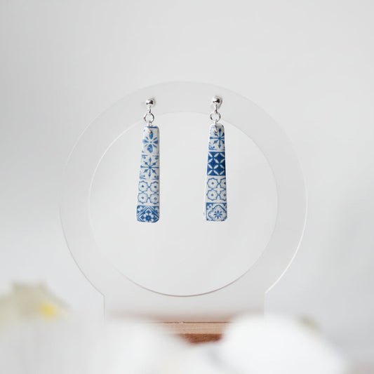 Pair of blue patterned earrings on a white circular stand with a blurred background