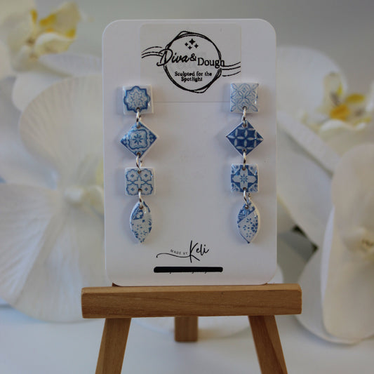 Set of blue floral earrings on a display card with a wooden stand.