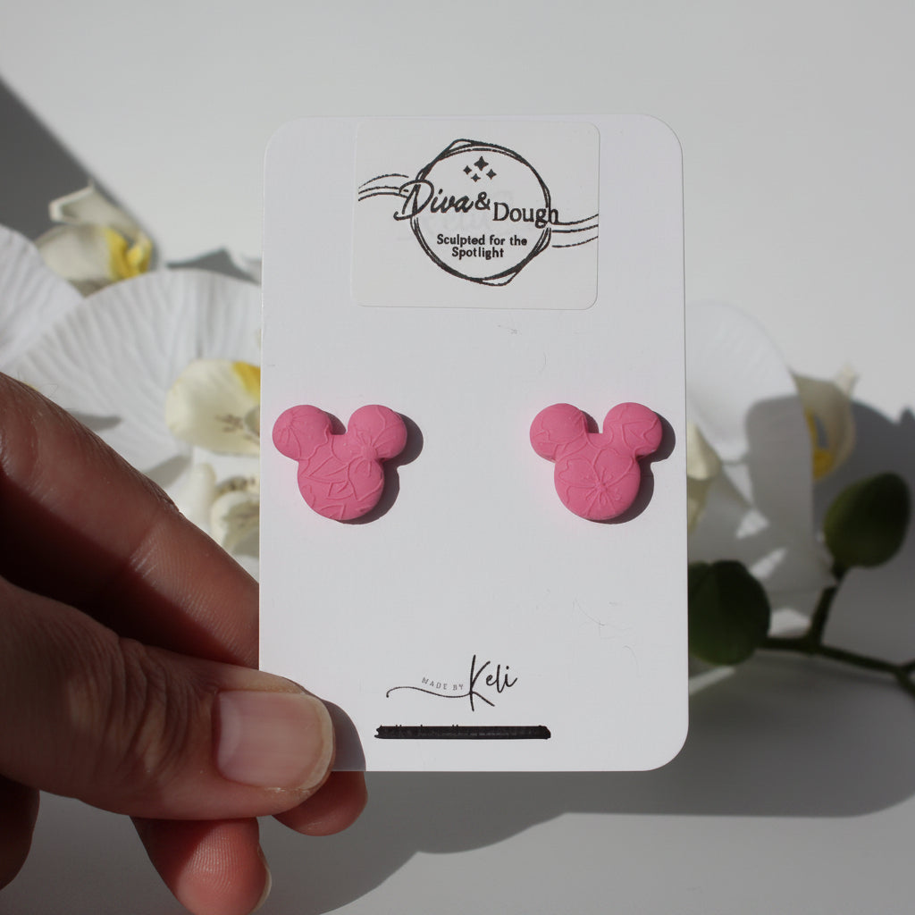 Pink mouse ear earrings on a branded card held by a hand with flowers in the background