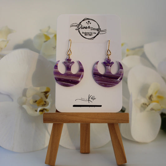 Purple earrings on a display card with a wooden stand against a white background