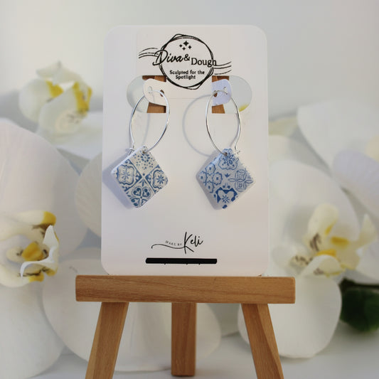 Pair of tile print earrings on a display card with a wooden stand against a white background