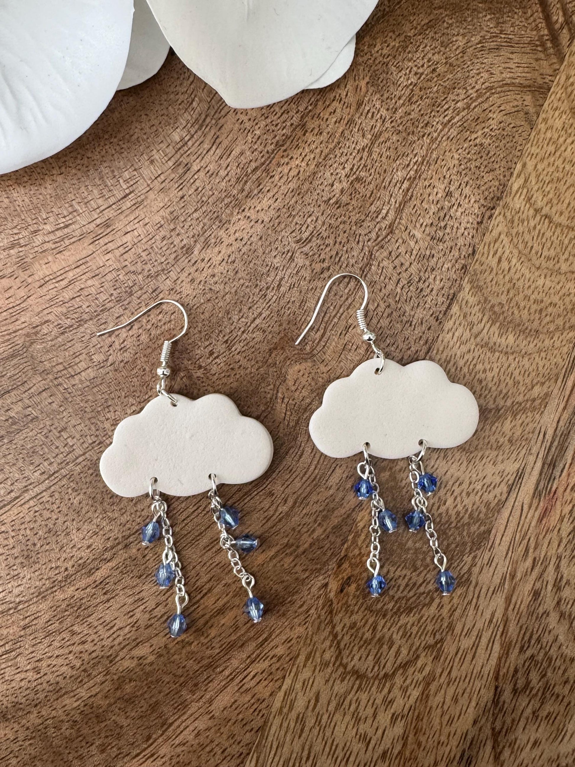 Cloud-shaped earrings with blue beads on a wooden surface
