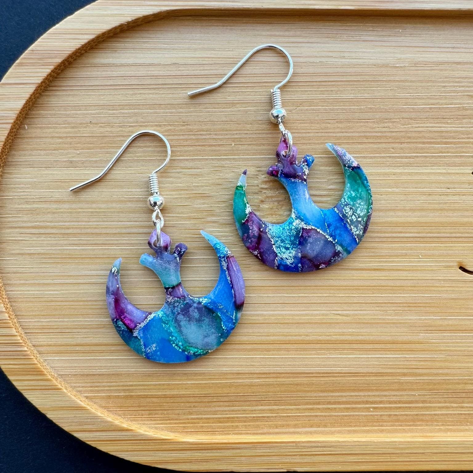 Colorful crescent moon-shaped earrings on a wooden tray with a dark background