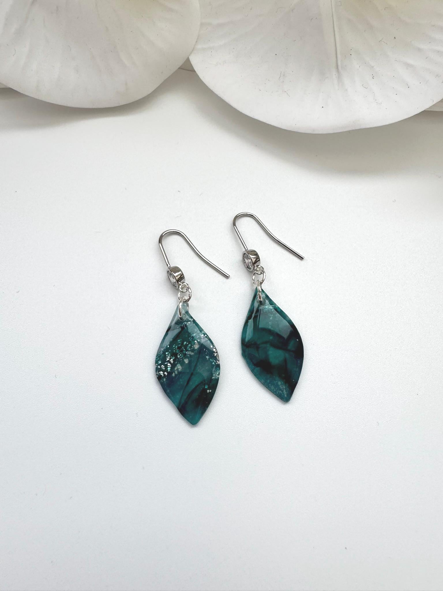 Teal earrings on a white surface with seashells in the background