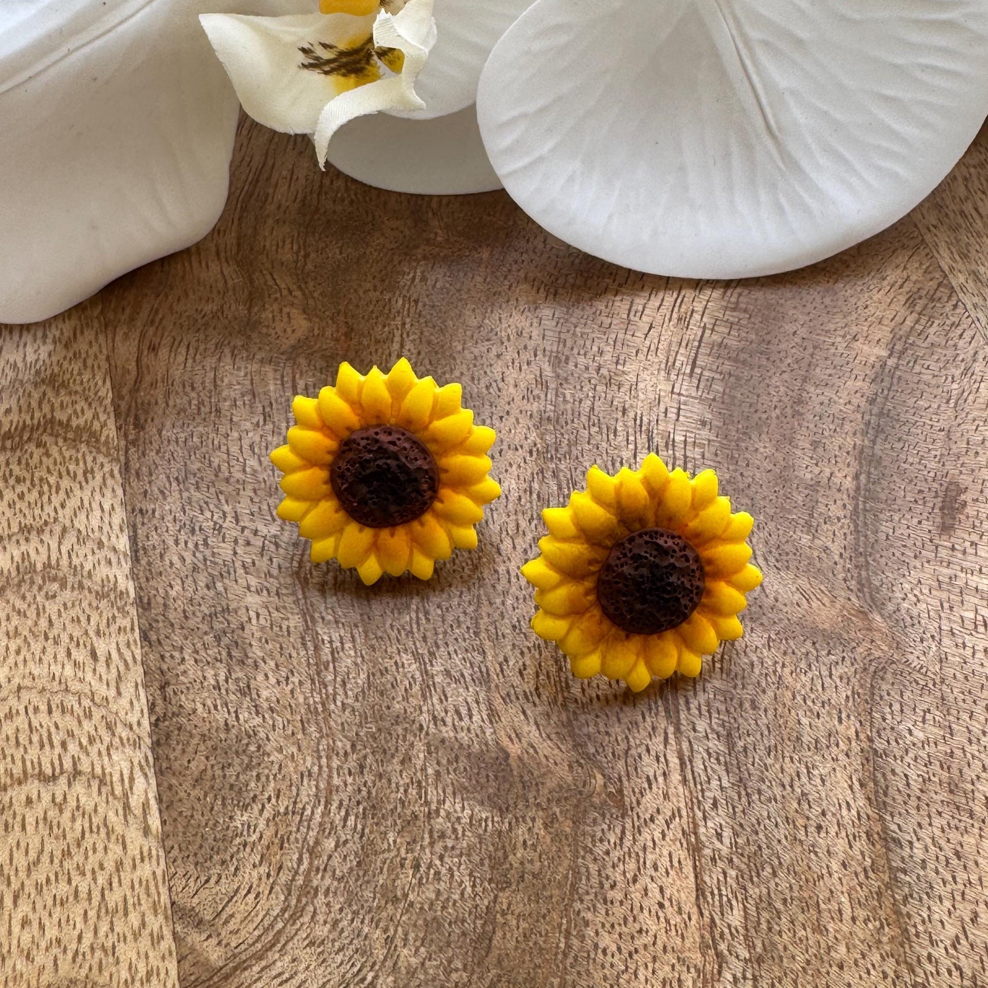 Yellow sunflower-shaped earrings on a wooden surface with white flowers in the background.