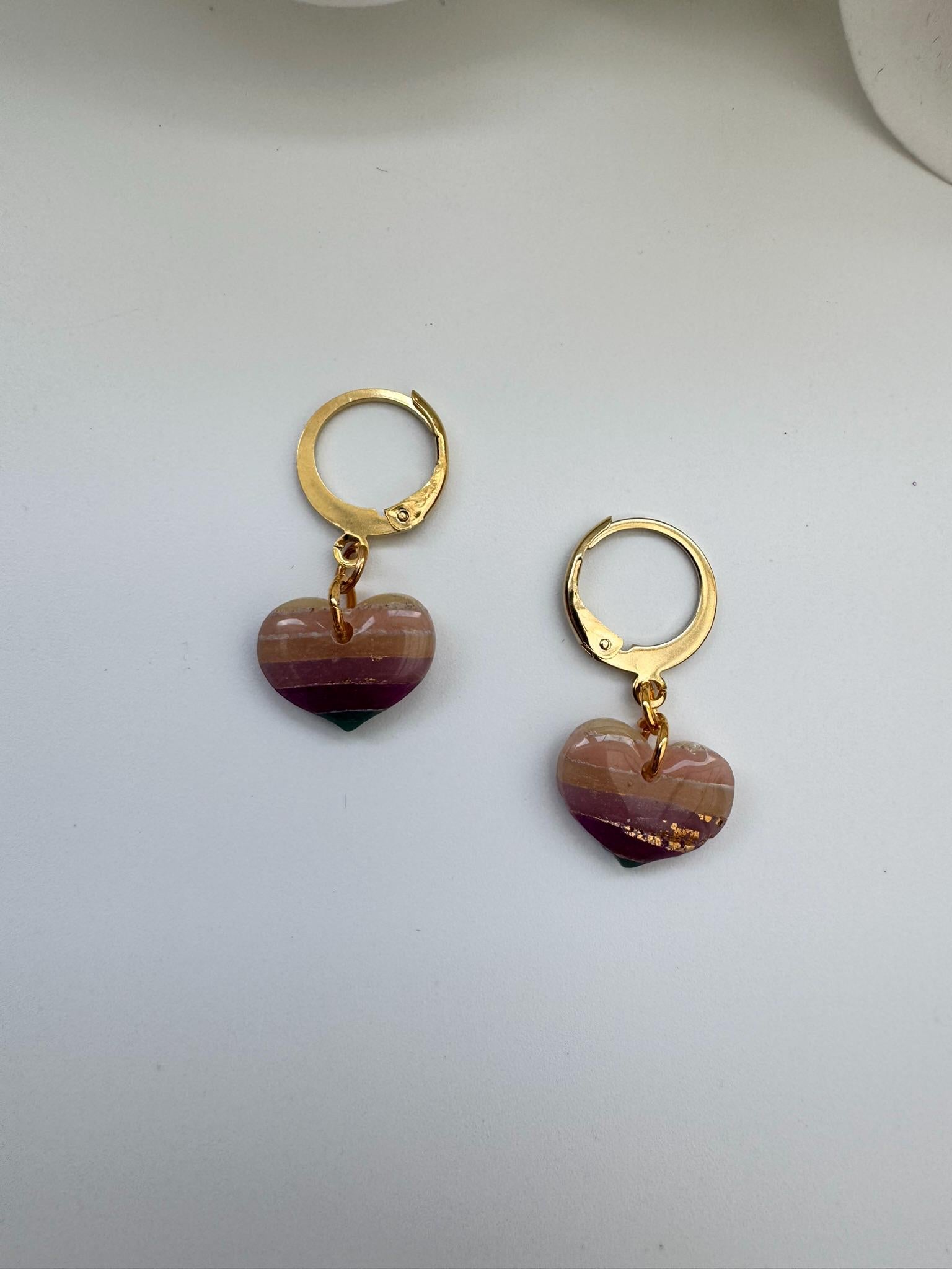 Gold hoop earrings with heart-shaped purple and green charms on a white background