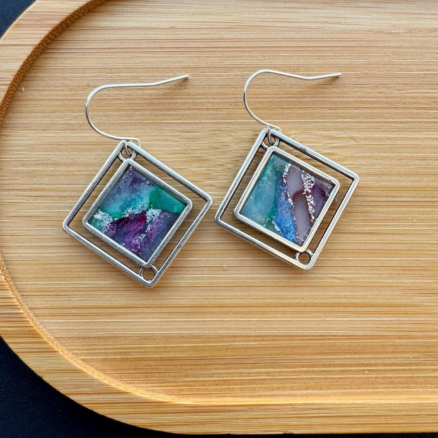 Square earrings with colorful stone inlays on a wooden tray