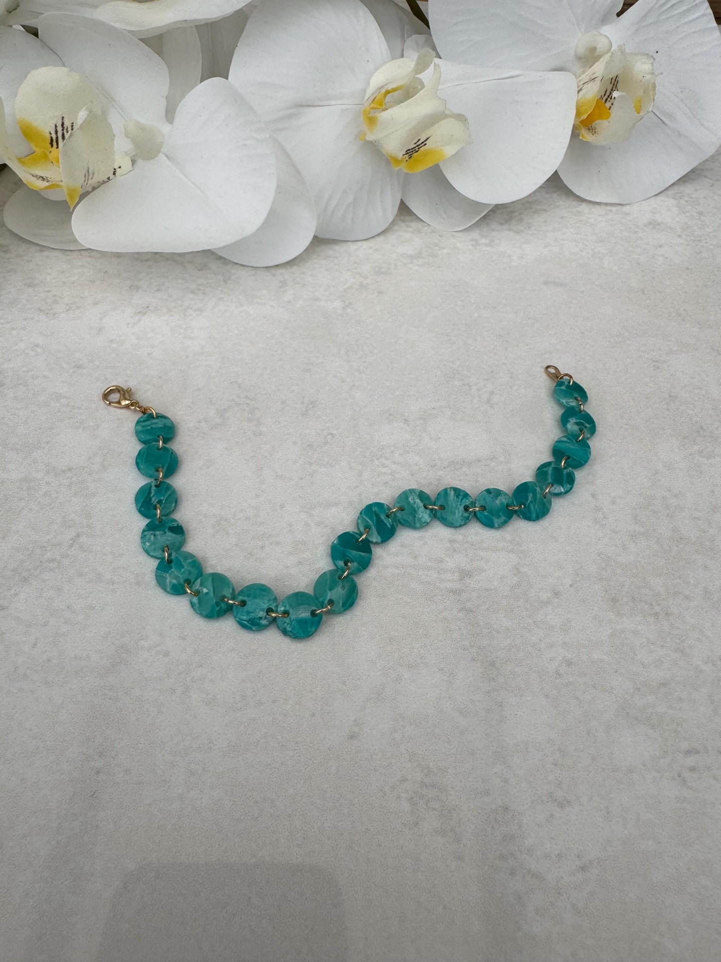 Teal beaded bracelet on a gray surface with white orchids in the background