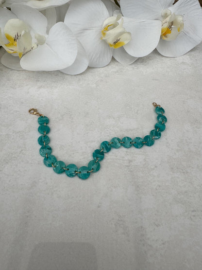 Teal beaded bracelet on a gray surface with white orchids in the background