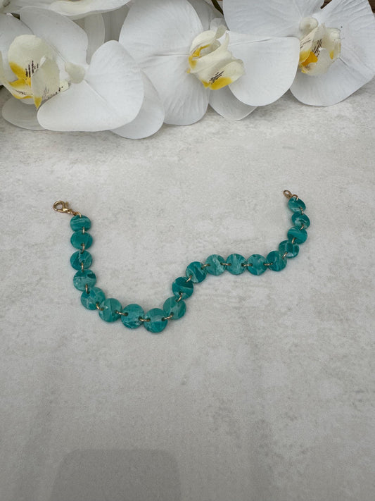Teal beaded bracelet on a gray surface with white orchids in the background