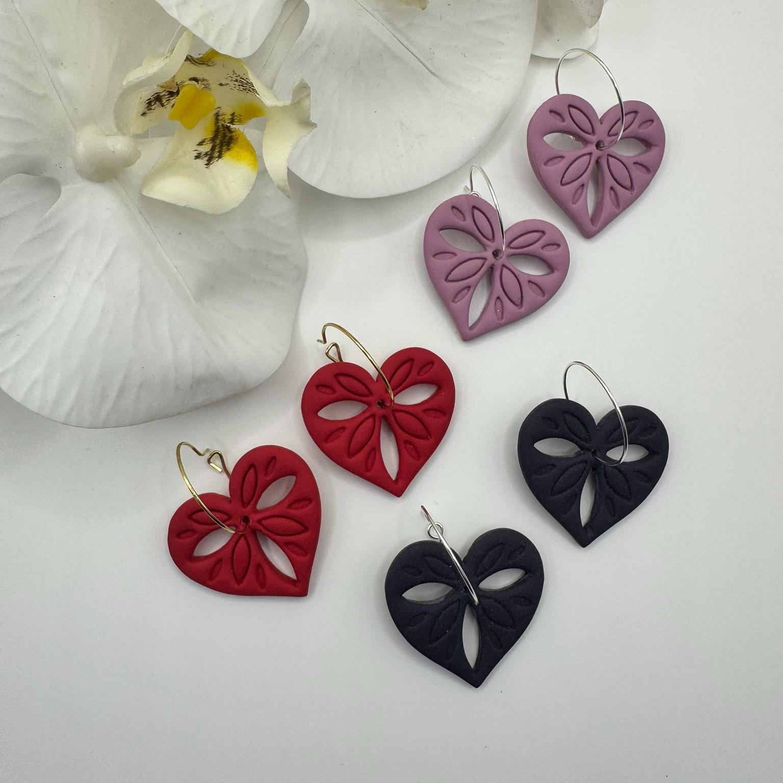 Heart-shaped earrings in red, black, and purple with a white orchid in the background.