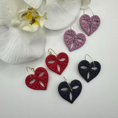 Heart-shaped earrings in red, black, and purple with a white orchid in the background.